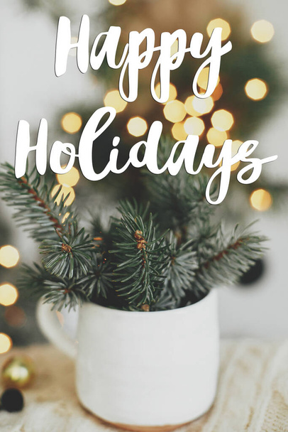 Kellemes ünnepeket szöveg csésze fenyő ágak kényelmes pulóver a háttérben a meleg fények. Varázslatos. A szezon üdvözlőlapja. Kézzel írott jel. Boldog karácsonyt!! - Fotó, kép