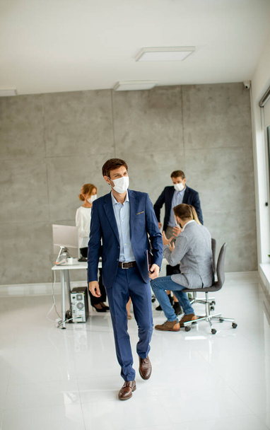 Schöner junger Geschäftsmann mit schützender Gesichtsmaske und digitalem Tablet im Büro - Foto, Bild