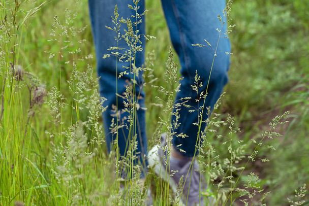 selectieve focus op benen van tienermeisje in jeans en paarse sneakers op weide. oncept van eenzaamheid en communicatie met de natuur - Foto, afbeelding