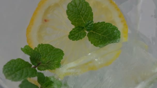 Δροσιστικό ανθρακούχο ποτό με μέντα και μια φέτα λεμόνι σε γυάλινο ποτήρι κοντά σε αργή κίνηση - Πλάνα, βίντεο