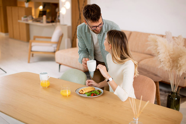 Schönes junges Paar spricht und lächelt, während es sich zu Hause gesund ernährt. - Foto, Bild