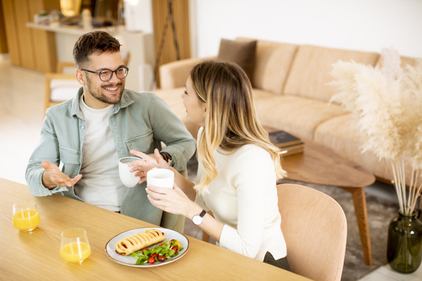 Hermosa pareja joven hablando y sonriendo mientras come sano en casa. - Foto, Imagen
