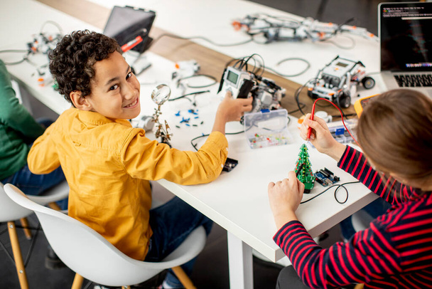 ロボット教室で電気玩具やロボットをプログラミングする幸せな子供たちのグループ - 写真・画像