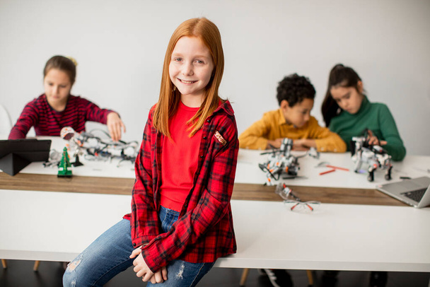Robot sınıfında elektrikli oyuncakları ve robotları programlayan bir grup çocuğun önünde duran sevimli küçük kız. - Fotoğraf, Görsel