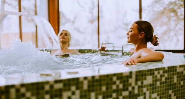 Pretty young women relaxing in the whirlpool bathtub at the poolside - 写真・画像