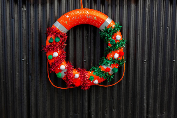 Una corona de Navidad hecha de una boya salvavidas colgando en público fuera de un club de vela - Foto, Imagen