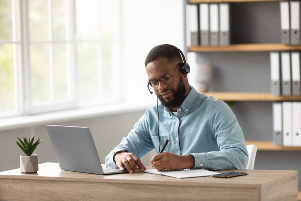 Зайнятий серйозний афроамериканський бородатий хлопець в окулярах і гарнітурах, що працюють на ноутбуці вдома
 - Фото, зображення