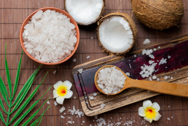 zeezout in een houten lepel met kokosnoot voor schoonheidsverzorging en mangobloemen  - Foto, afbeelding