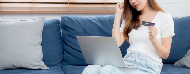 Młoda azjatycka kobieta siedzieć na kanapie za pomocą laptopa zakupy online z karty kredytowej zakupu do Internetu, happy girl płatności z e-biznesu na kanapie, zakup i płatność, koncepcja biznesu. - Zdjęcie, obraz