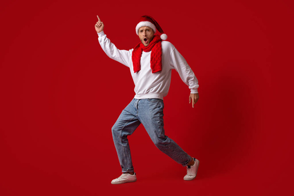Cheerful Young Man In Santa Hat Fooling Over Red Studio Background - Photo, Image