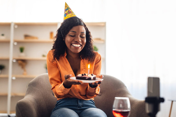 African Woman Holding anniversaire gâteau appel vidéo par téléphone à l'intérieur - Photo, image