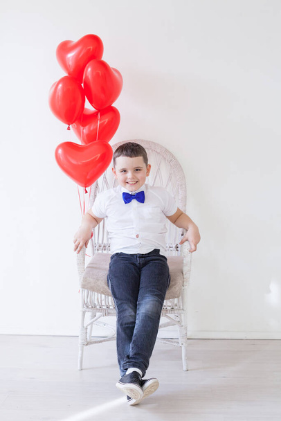μικρό αγόρι κάθεται σε μια καρέκλα με κόκκινα μπαλόνια - Φωτογραφία, εικόνα