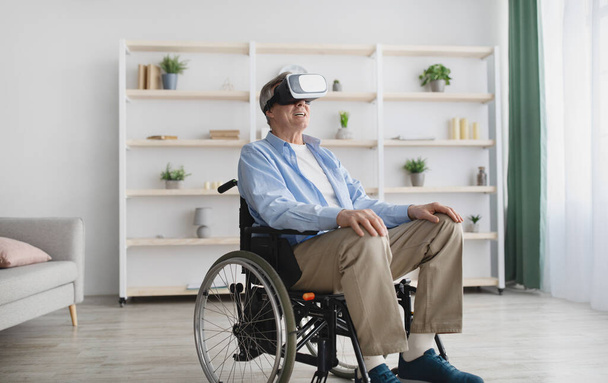 Hombre mayor feliz en silla de ruedas con gafas VR, jugando videojuego en línea en el ciberespacio en casa - Foto, Imagen