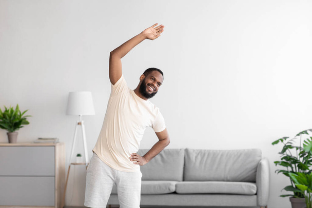 Happy young african american man with beard in white sportswear doing exercise and warm-up - Photo, Image