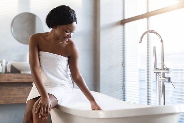 Pozytywny atrakcyjny czarny lady siedzi na kąpieli w nowoczesnej łazience - Zdjęcie, obraz