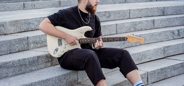 Young street musician playing guitar sitting on granite steps - Foto, Bild