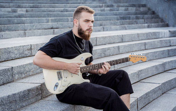 Young street musician playing guitar sitting on granite steps - Foto, Imagen