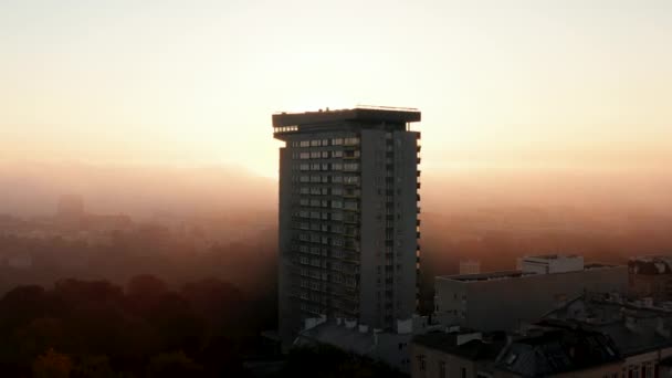 Лети над самотнім багатоквартирним будинком у місті. Висхідне сонце в тумані. Ранок пробився крізь розріджений туман або низькі хмари. Варшава, Польща - Кадри, відео