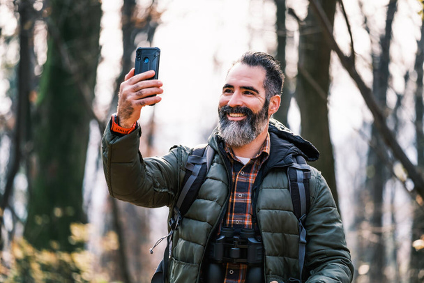 Image of man enjoys hiking and making selfie with his phone. - Foto, afbeelding