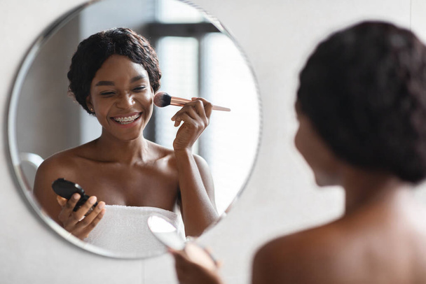 Красивая черная леди наносит макияж в ванной комнате - Фото, изображение