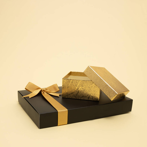 パステルベージュの背景に黒と金色のギフトボックス。クリスマスと新年の作曲。最小限の休日の概念. - 写真・画像