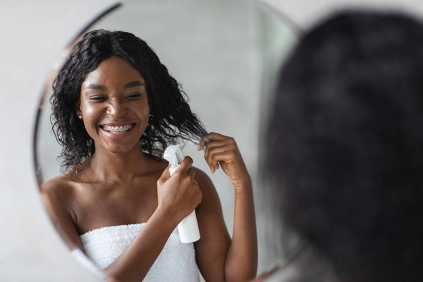 Felice giovane donna nera utilizzando lacca per capelli - Foto, immagini