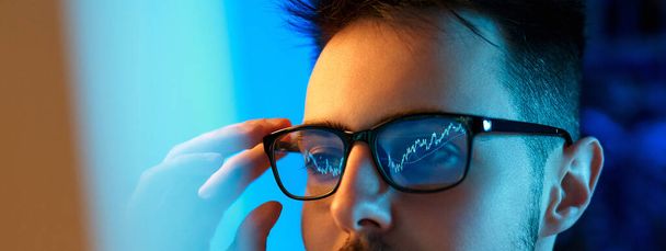 Close up of Caucasian young salesman wearing glasses looking at monitor with graphs while working in office. Stock trading, people, business concept. - Foto, Imagem