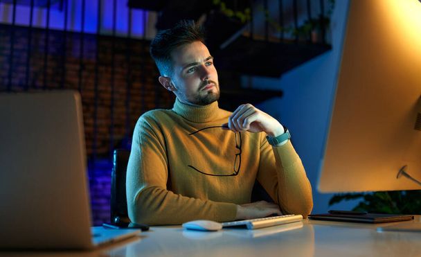 Серьезный бизнесмен, сидящий в офисе поздно ночью после работы, работает за компьютером и ноутбуком. Фрилансер, работающий из дома по ночам. - Фото, изображение