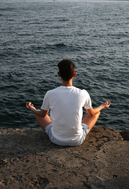 Spor giyimli bir gencin portresi gün doğumunda deniz kenarındaki bir rıhtımda meditasyon yapıyor. Sporcu adam okyanus tarafından meditasyona tabi tutulur. - Fotoğraf, Görsel