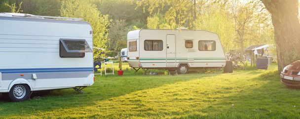 Wohnwagenanhänger und ein Auto, das auf einer grünen Wiese auf einem Campingplatz abgestellt ist. Idyllische Frühlingslandschaft. Holland. Wohnmobil, Transport, Roadtrip, Urlaub, Ökotourismus, Reisen, Lifestyle, Erholung - Foto, Bild