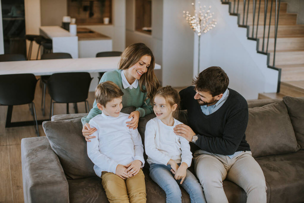 Szczęśliwa młoda rodzina z dwójką dzieci cieszyć się razem na kanapie w salonie - Zdjęcie, obraz