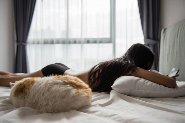 ベッドの上でスマートフォンでチャット、テキスト、ソーシャルメディアを再生し、そのトップレスセクシー所有者とエキゾチックなショートヘア猫を寝ています。朝服を着る前にシャワーを浴びてリラックスした. - 写真・画像