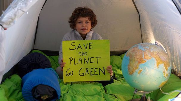 Italia, Milán, Activista niño 7 años con signo Save the Planet, ir verde - Viernes para la Juventud Futura 4 Clima - niño acampando en casa en tienda de campaña durante el bloqueo del Covid-19 Coronavirus - no planeta B - Foto, Imagen