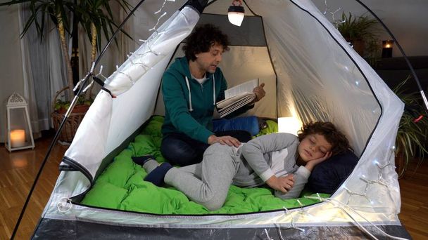 Italia, Milano - Papà uomo mette a dormire il figlio e leggere una favola in tenda campeggio a casa durante Covid-19 Coronavirus isolato epidemia - stile di vita in famiglia padre e figlio - desiderio di viaggiare - Foto, immagini