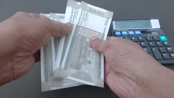 Lidská ruka počítající 500 rupiových indických bankovek proti kalkulačce a peru umístěnému na stole. Vysoký úhel pohledu. Zavřít. Pozadí financování bankovnictví. - Záběry, video