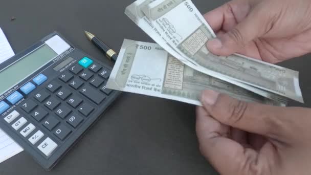 Ihmisen käsi laskee uutta 500 rupian Intian valuutan seteliä laskimeen ja kynään, joka on asetettu pöydälle. Korkeassa kulmassa. Sulje se. Pankkien rahoituksen taustaa. - Materiaali, video