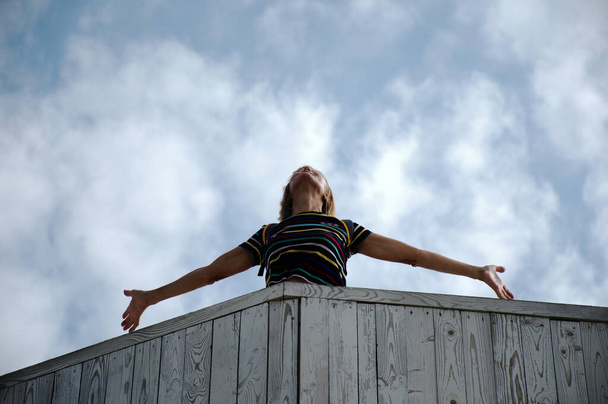 Szczęśliwego lotu. Kobieta z wyciągniętymi ramionami stoi na drewnianym balkonie. Jej twarz jest zwrócona ku niebu.  - Zdjęcie, obraz