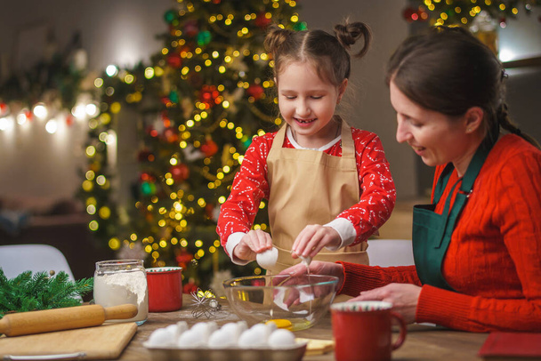 Merry Christmas. My daughter helps my mother cook. Family cooking of festive food. Mother and daughter are making Christmas cookies. happy holidays. Evening time, happy family in the kitchen. - Zdjęcie, obraz