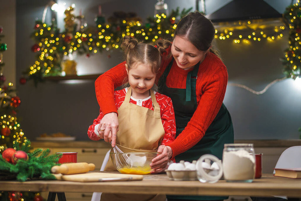 Merry Christmas. My daughter helps my mother cook. Family cooking of festive food. Mother and daughter are making Christmas cookies. happy holidays. Evening time, happy family in the kitchen. - Zdjęcie, obraz