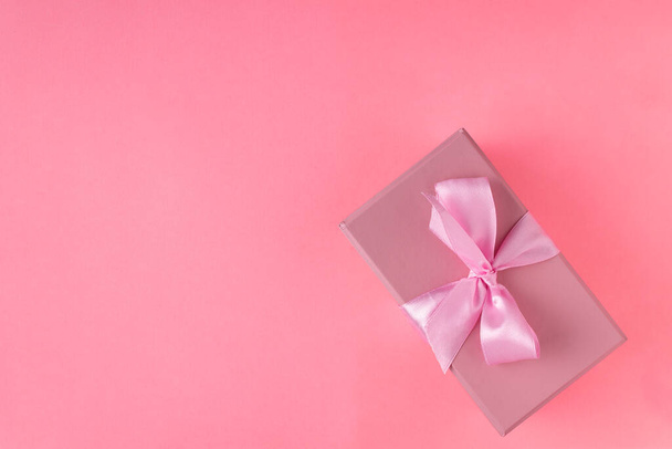 vaaleanpunainen lahjapakkaus sidottu satiininauhalla vaaleanpunaisella taustalla - Valokuva, kuva