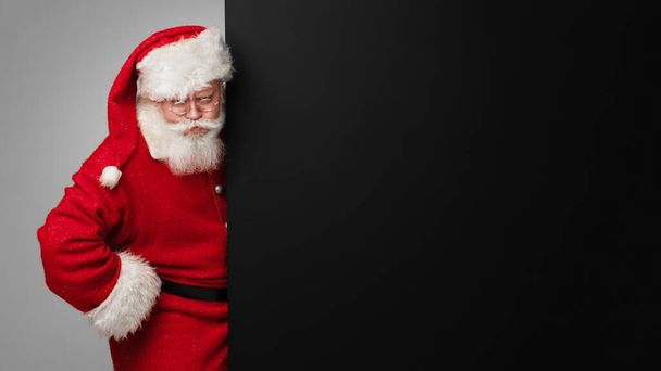 Santa Claus with black paper billboard with copy space for text , surprised facial expression - Фото, изображение
