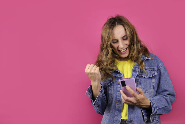 happy excited girl with a smartphone, got good news on phone, in casual clothes on a pink background - Photo, Image