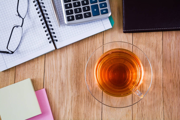 Egy csésze tea, jegyzetfüzet tollal, számológéppel és poharakkal az asztalon. Üzleti koncepció - Fotó, kép