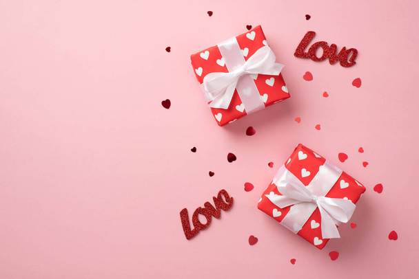 Top view photo of valentine's day decorations two gift boxes in red wrapping paper with pattern of hearts and bows inscriptions love and confetti on isolated pastel pink background with copyspace - Foto, imagen