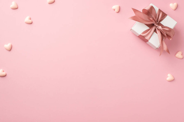 Вид зверху фото прикрас дня Валентина біла подарункова коробка з рожевим атласною стрічкою лук і маленькі серця на ізольованому пастельно-рожевому фоні з порожнім простором
 - Фото, зображення