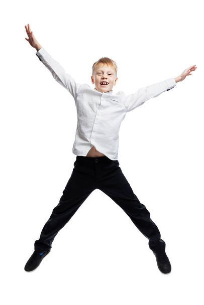 The joyful boy is jumping. The guy in trousers and a white shirt. Activity and movement. Full height. Isolated on white background. Vertical. - Fotó, kép
