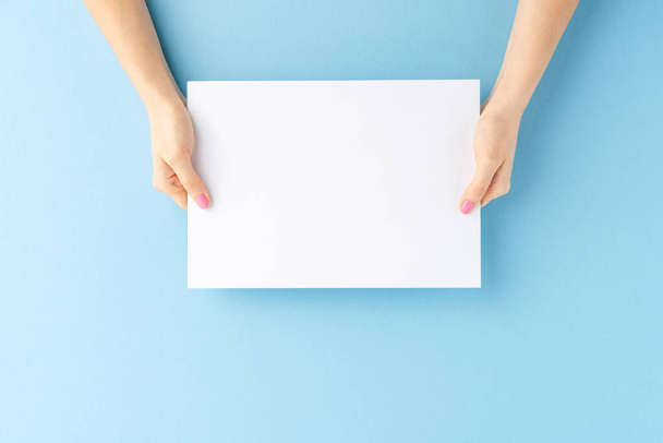Young female hands showing empty white paper sheet on blue background. Mockup - Фото, изображение
