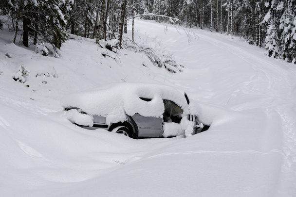 Ασημένιο αυτοκίνητο εγκαταλείφθηκε και εγκαταλείφθηκε στο χαντάκι ενός επαρχιακού χωματόδρομου στο δάσος. Καλυμμένο με βαθύ χιόνι - Φωτογραφία, εικόνα