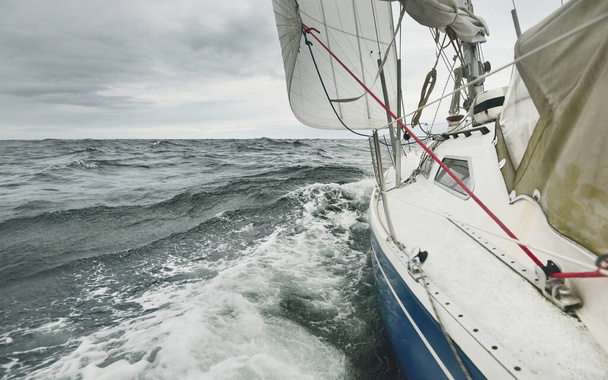 Яхт пливе під час грози в дощовий день. Вигляд зблизька з палуби на лук, щогла і вітрила. Драматичне штормове небо, темні хмари. Хвилі та вода бризкають. Важка погода. Балтійське море, Швеція - Фото, зображення