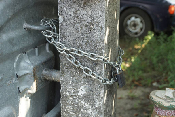 chaîne en fer gris avec cadenas noir sur un pilier en béton à l'extérieur - Photo, image